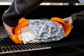 Bright orange silicone grill mitts protecting hands while handling hot food on outdoor grill in grilling accessories collection