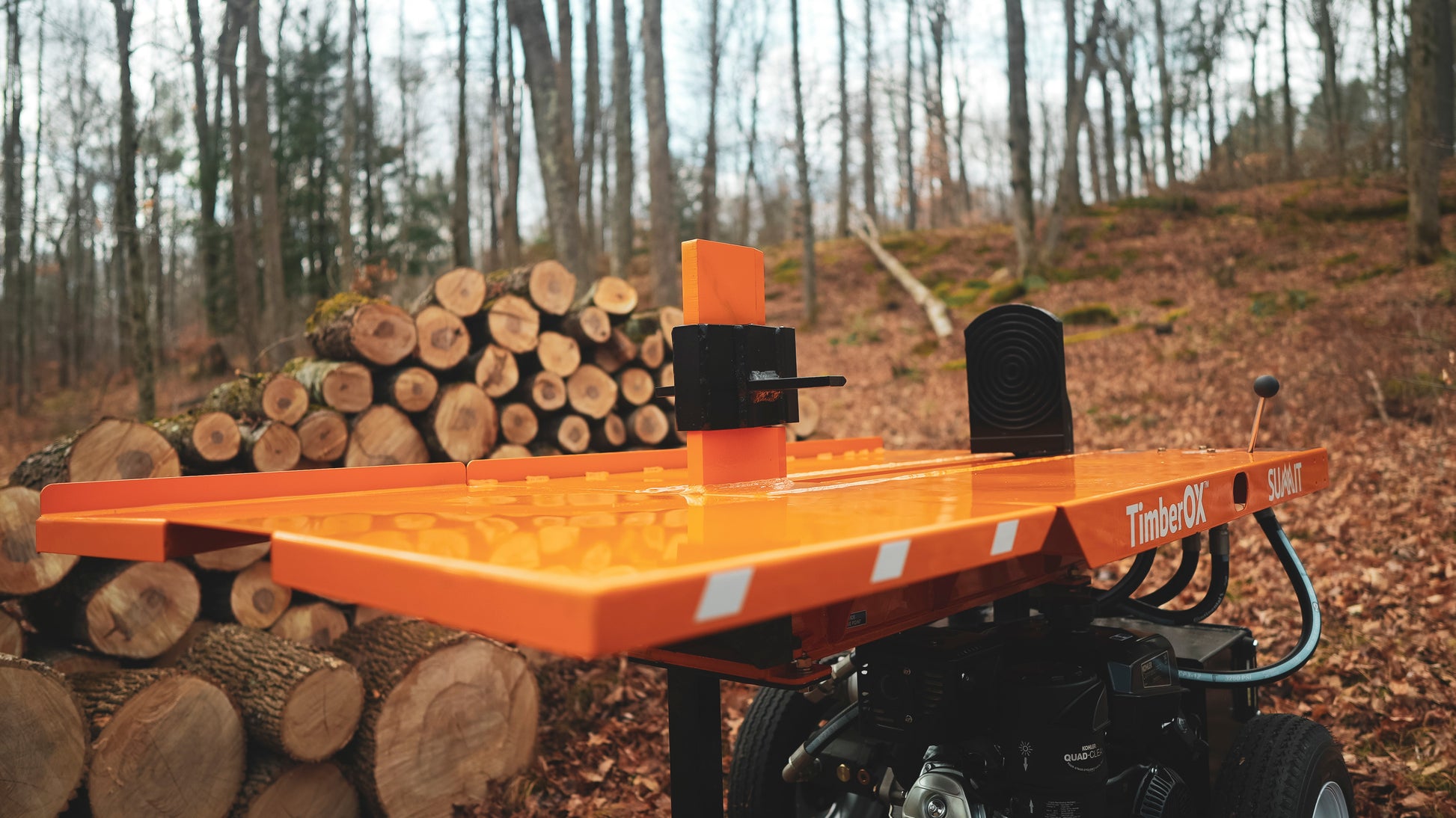 Orange LogOx TimberOX Summit 30-ton log splitter with black engine next to stacked cut logs in forest setting for home improvement tasks