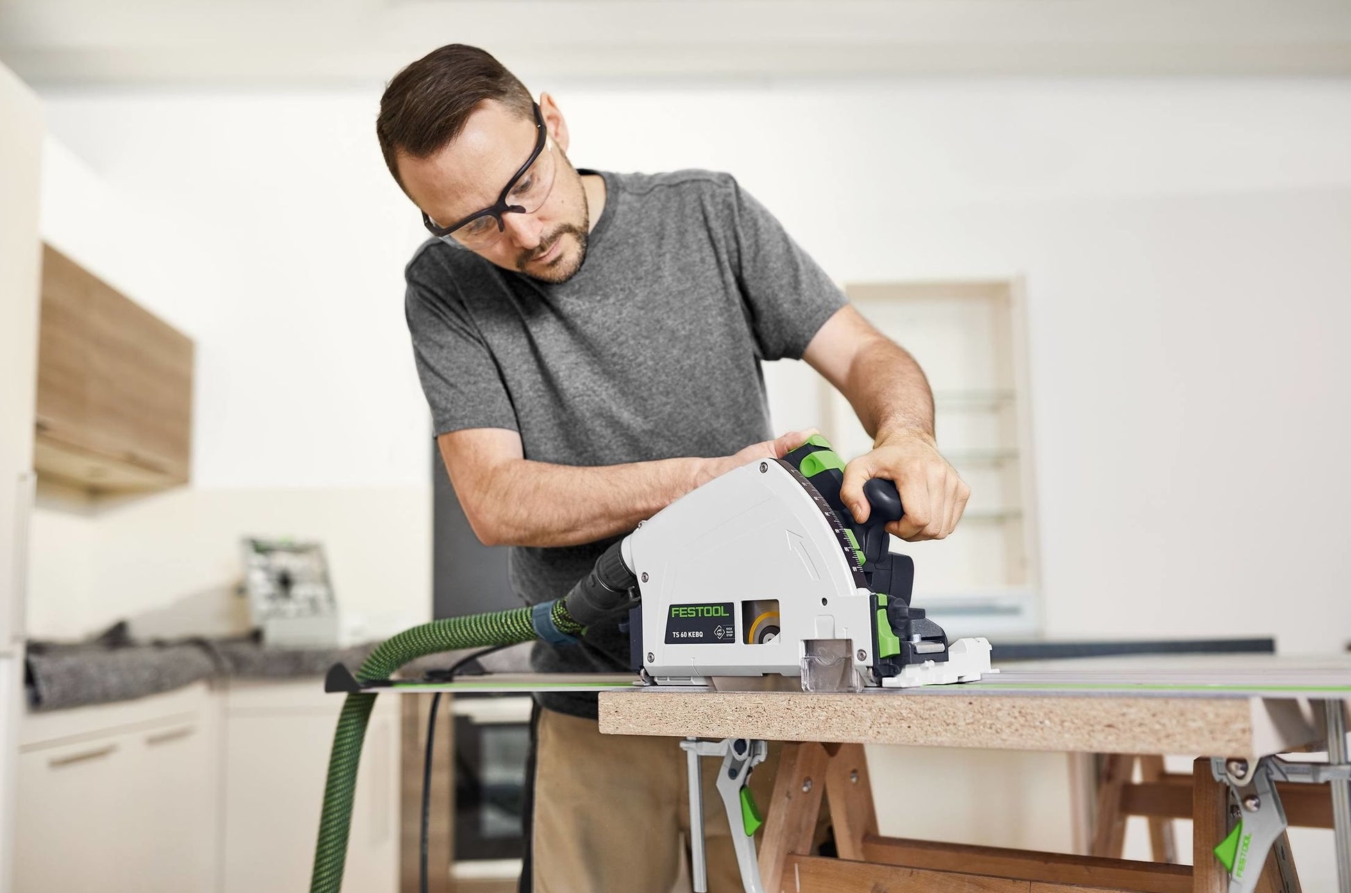 Man using Festool plunge cut track saw on wood panel in home improvement workspace with protective glasses