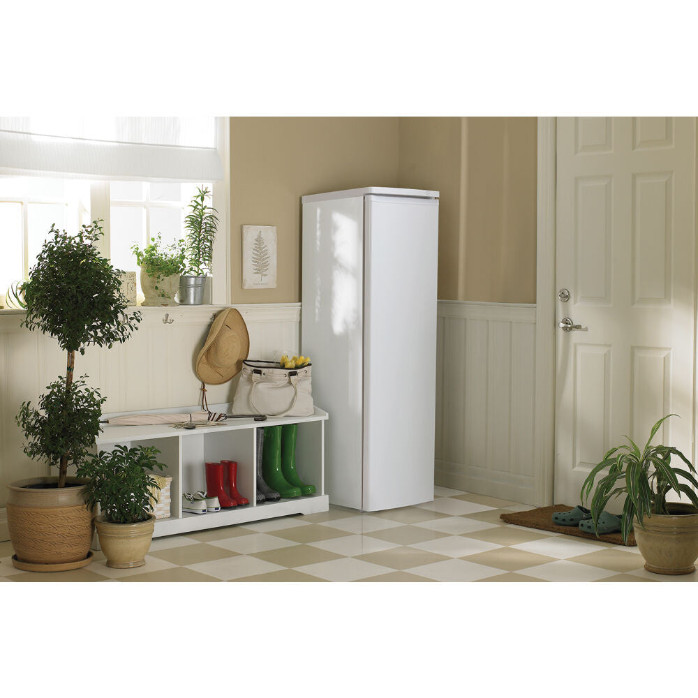 White upright freezer with single door and recessed handle in a bright kitchen corner with plants and storage bench