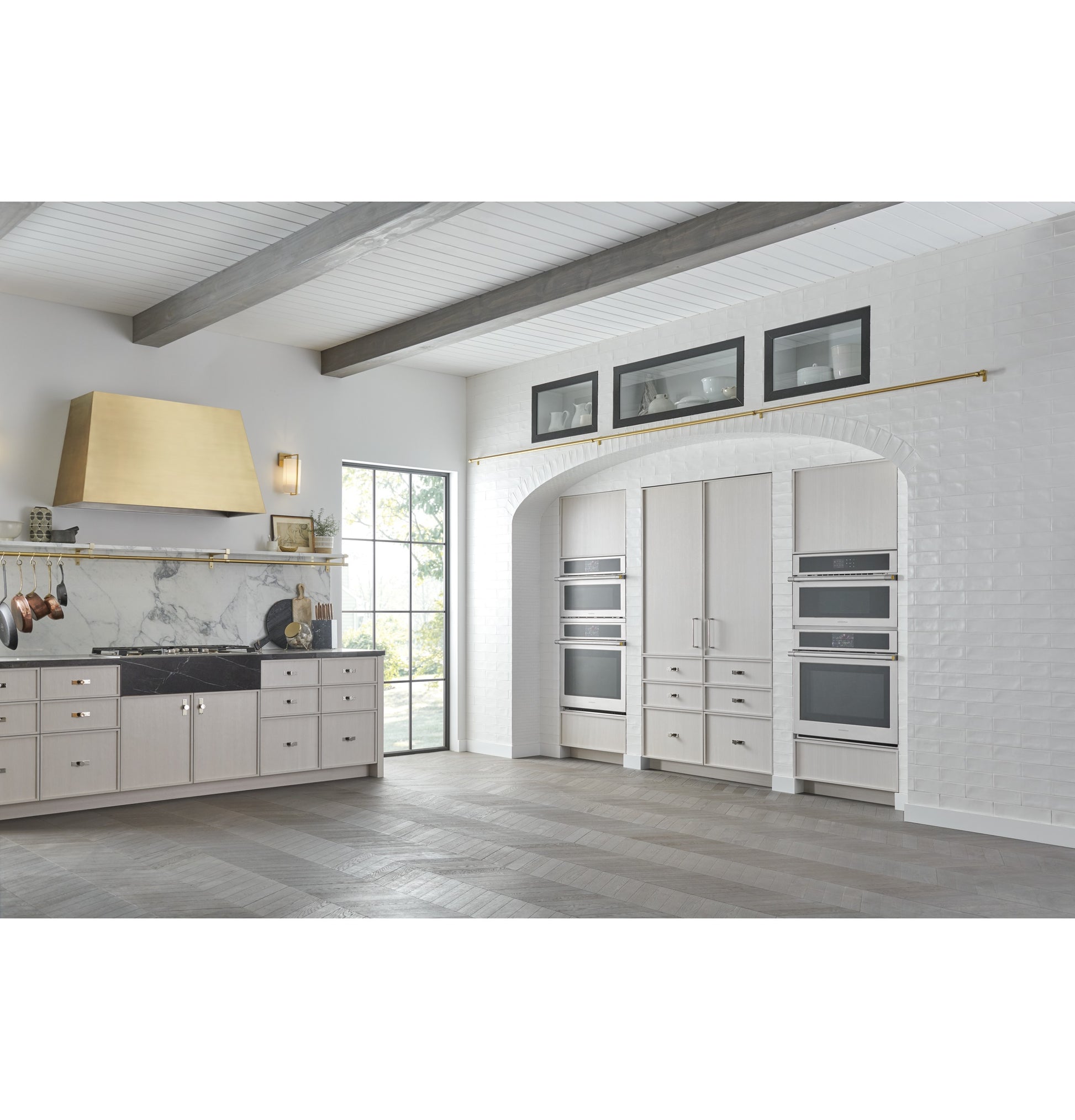 Modern kitchen with built-in steam oven and multiple wall ovens in white brick and wood flooring, appliances collection