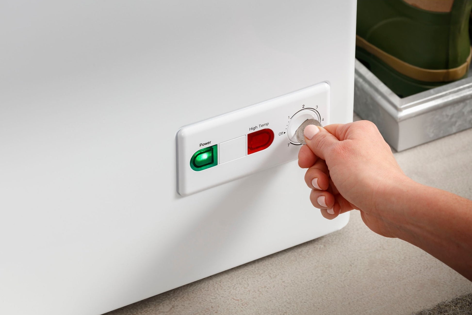 Hand adjusting temperature dial on white manual defrost chest freezer with green and red indicator lights in home setting
