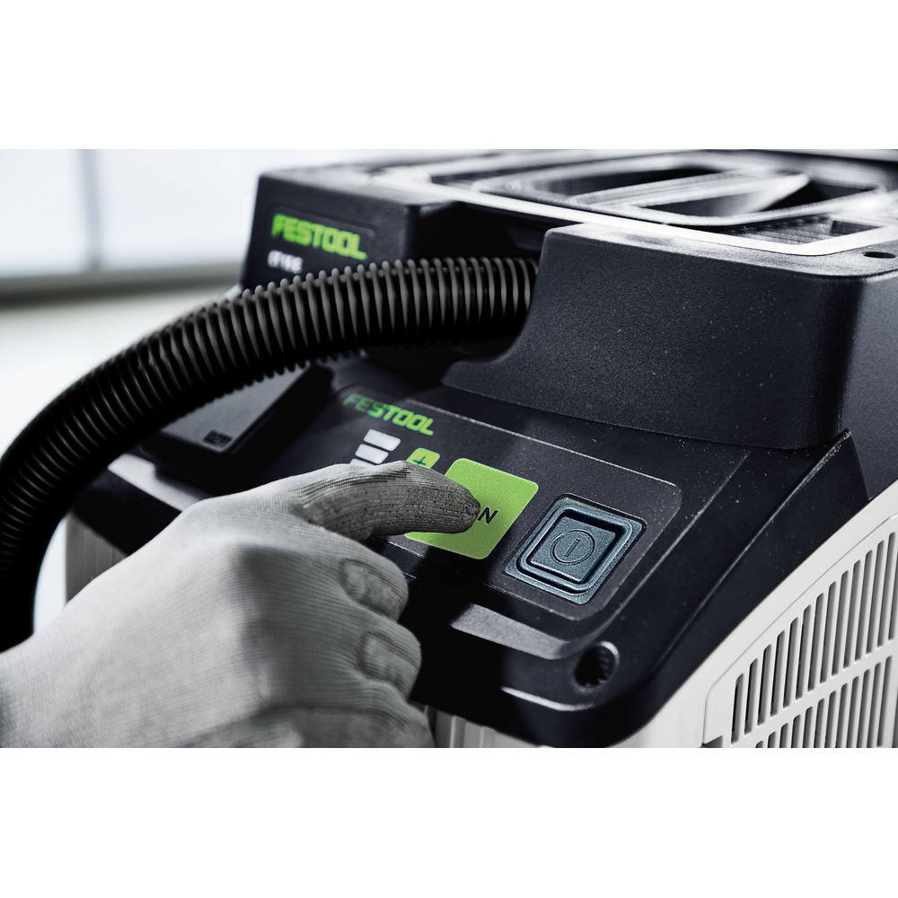 Close-up of a gloved hand pressing the green start button on a Festool HEPA dust extractor for tools and home improvement tasks