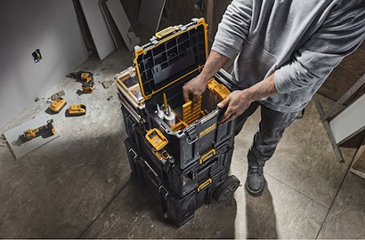 Worker organizing a stackable yellow and black DEWALT tool chest with multiple compartments on a jobsite floor