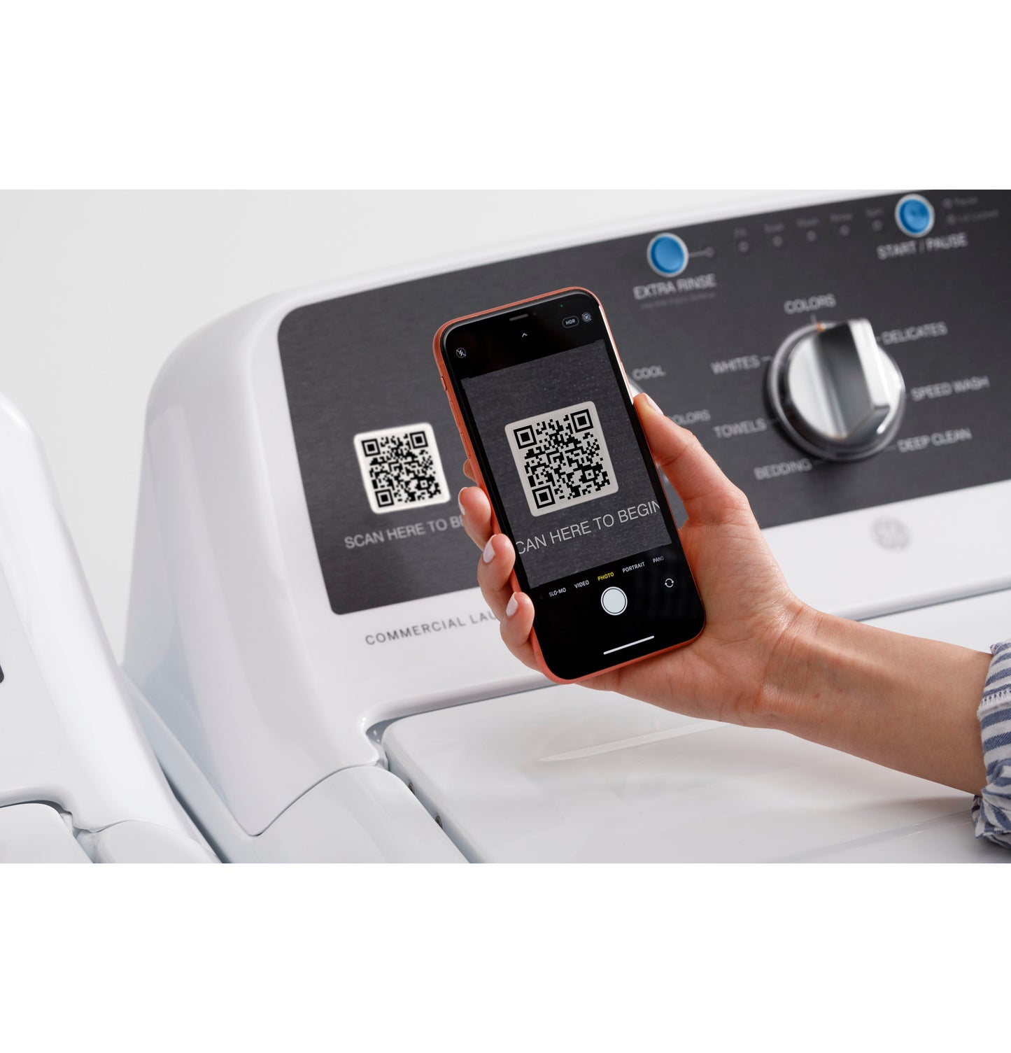 Hand holding smartphone scanning QR code on control panel of white commercial top load washer from washers collection