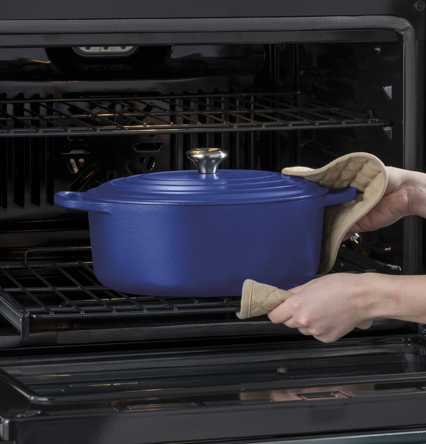 Person using oven mitts to place a blue cast iron pot into a built-in convection double wall oven interior