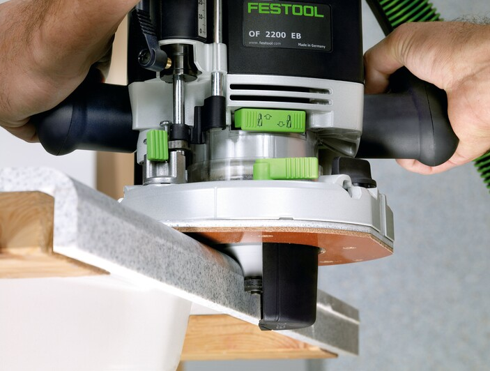 Hands holding Festool router with green adjustment knobs on woodworking project in home improvement tool setup