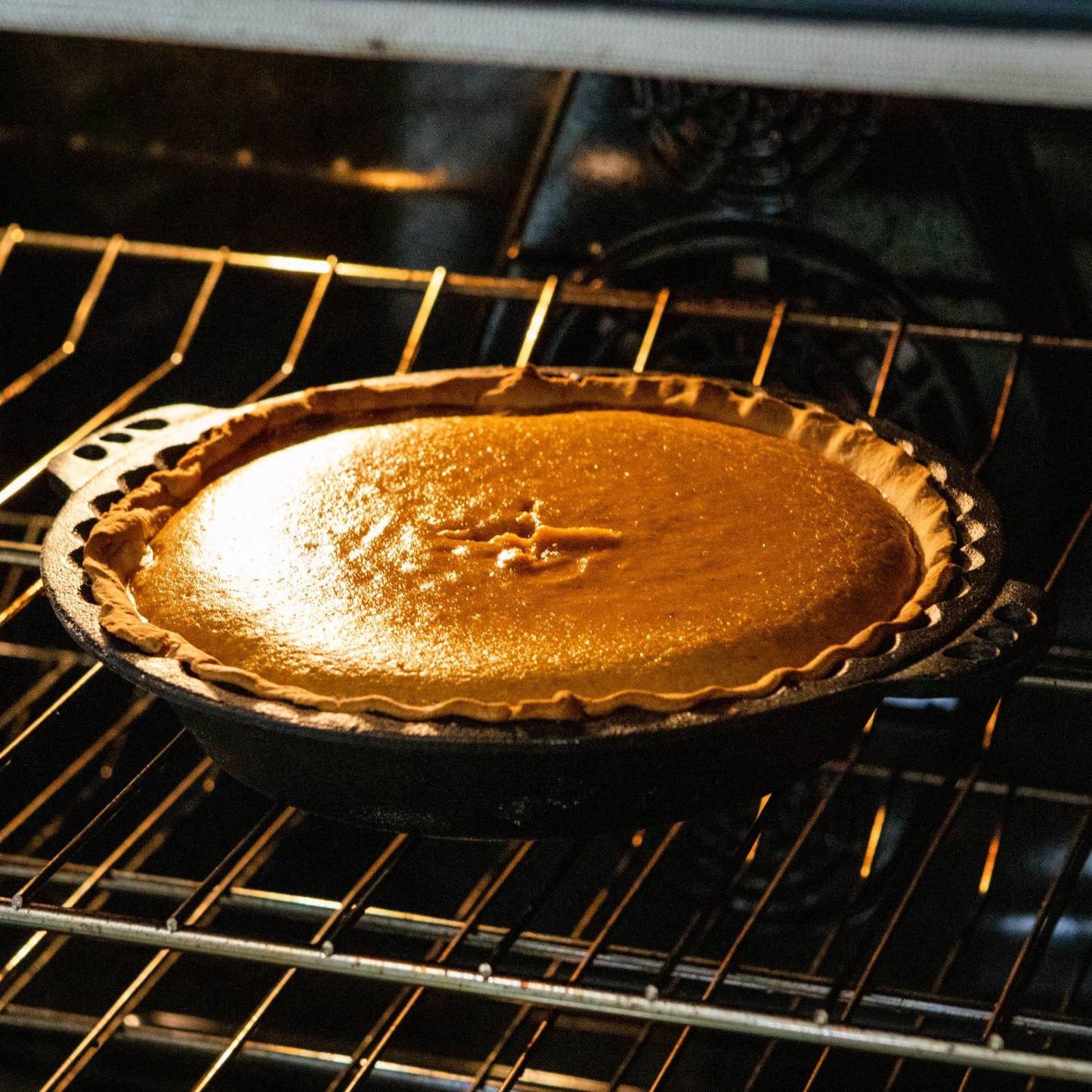 Pumpkin pie baking in cast iron pan with crimped edges inside an oven for kitchenware collection under $50