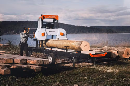 Portable band sawmill cutting large logs outdoors near a lake with a user operating the machinery