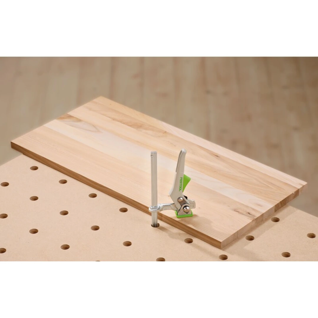 Quick clamp with green handle securing a wooden board on pegboard workbench in woodworking tool accessories collection