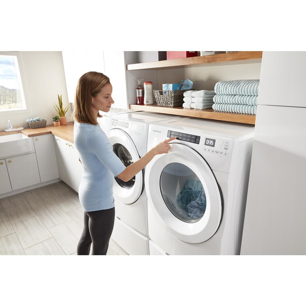 Woman operating white front load washer and dryer set elevated on storage pedestals in modern laundry room