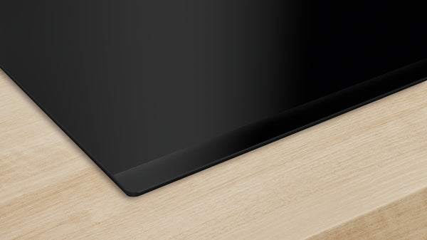 Corner view of sleek black induction cooktop surface installed on light wood countertop from Bosch Appliances collection