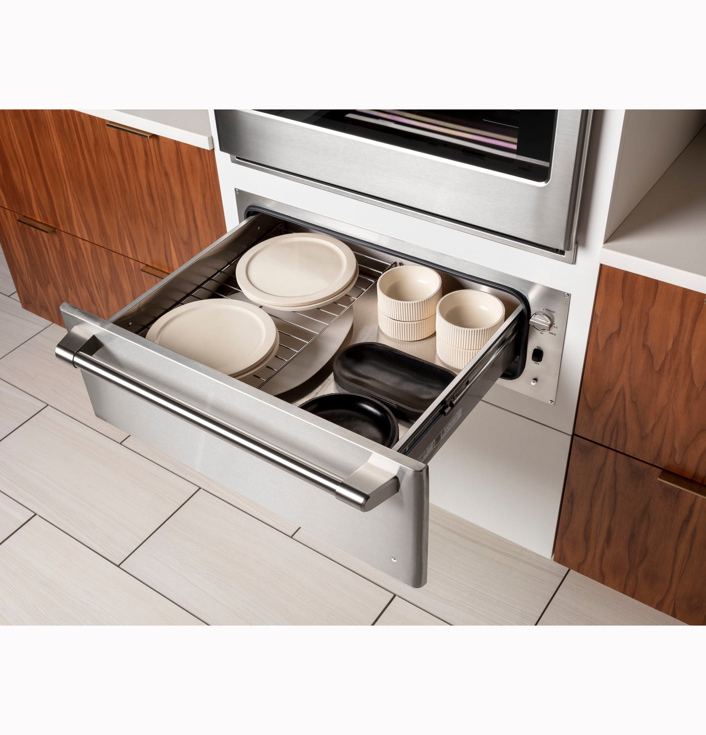 Built-in stainless steel warming drawer with dishes and serving bowls in modern kitchen and wall ovens collections