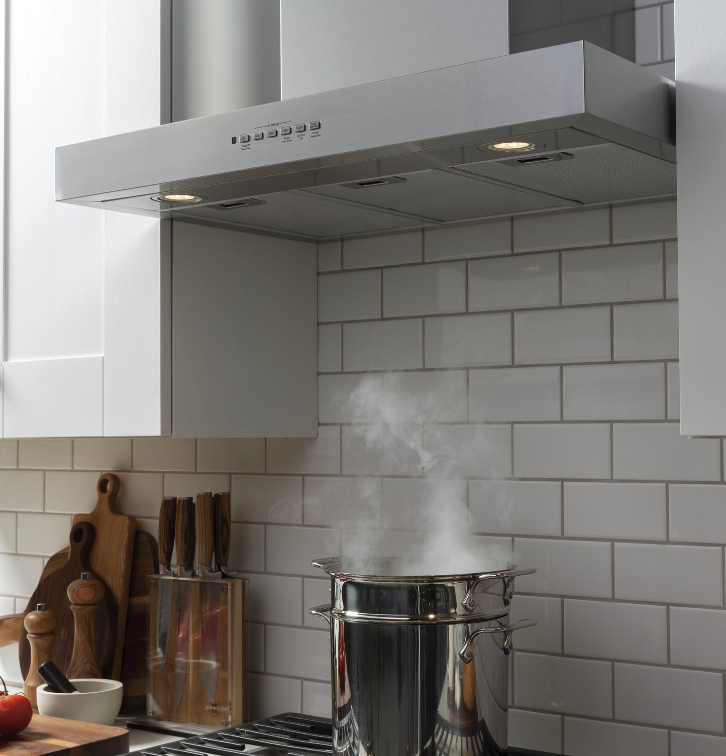 Stainless steel wall mount hood with dimmable LED lights over stovetop steaming pot in modern kitchen setting