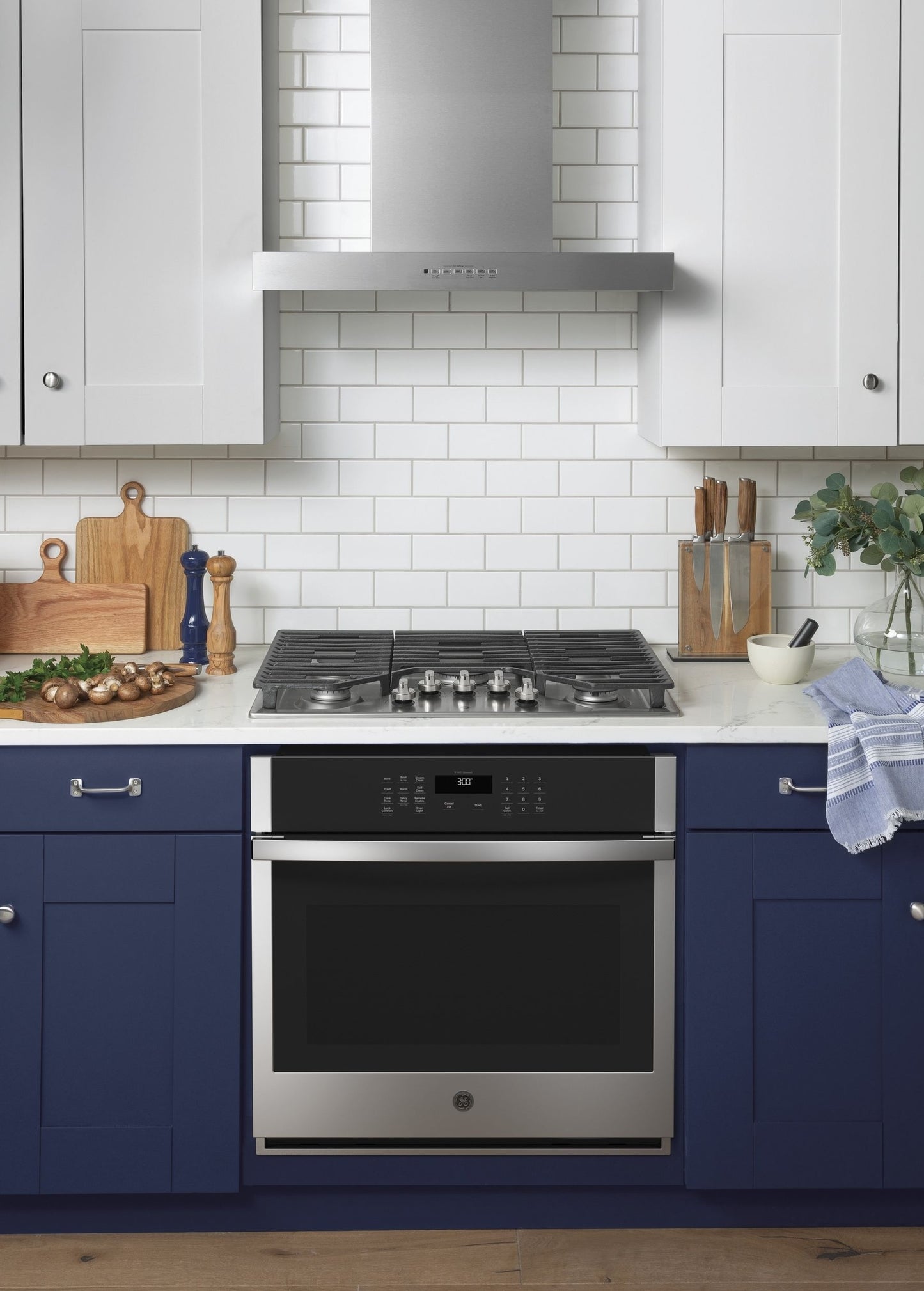 Modern kitchen with stainless steel wall mount range hood, blue lower cabinets, and gas cooktop with built-in oven