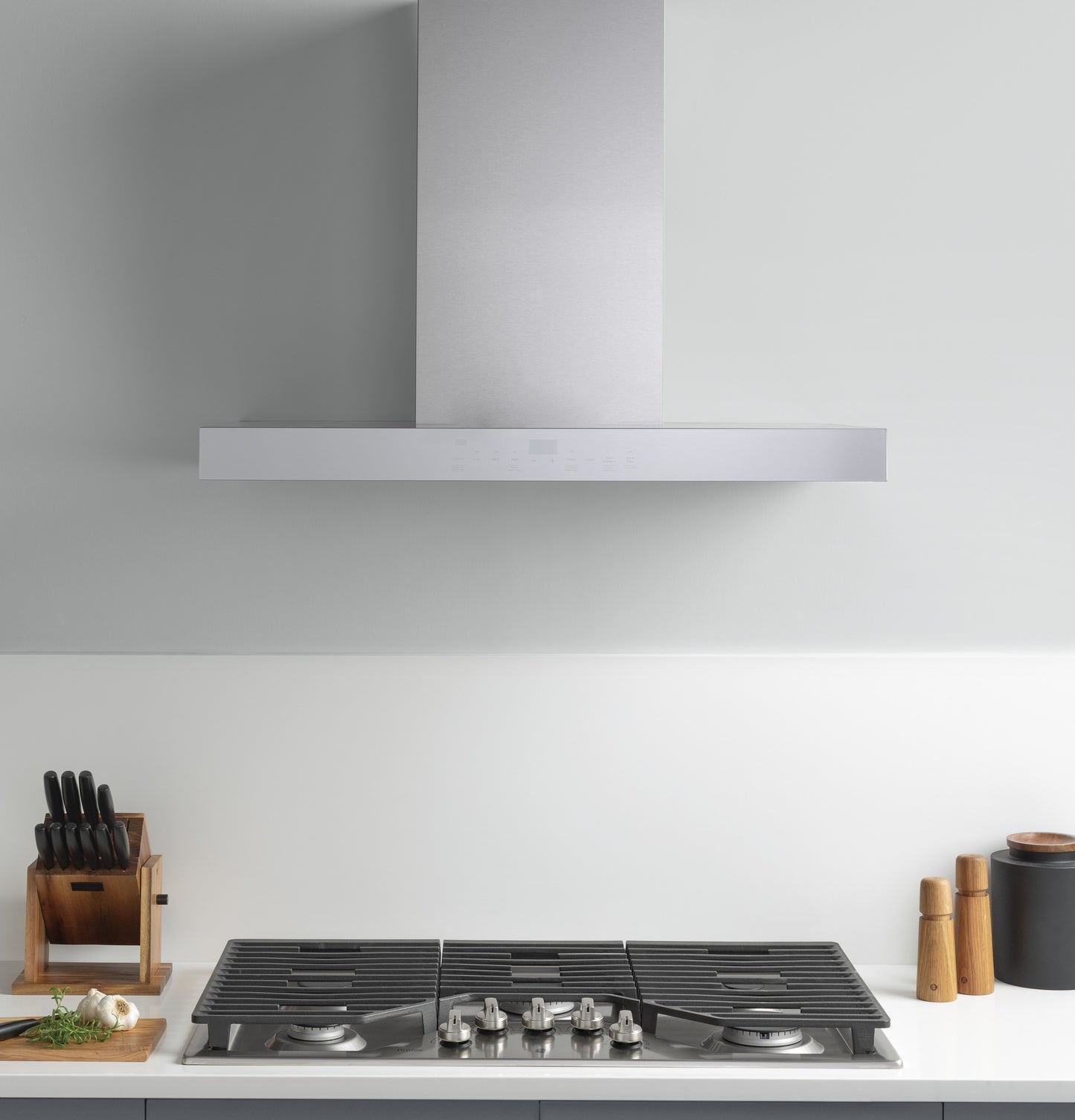 Modern stainless steel gas cooktop with five burners beneath a sleek built-in range hood in a minimalist kitchen setting