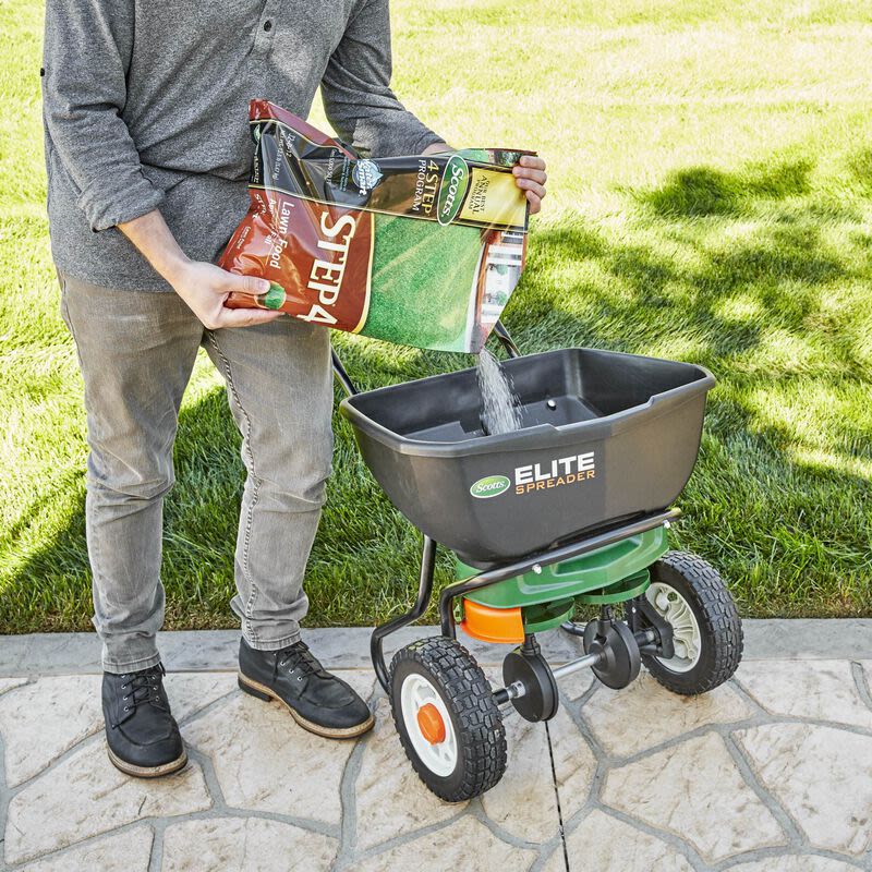 Pouring Scotts branded fall lawn food into a black Elite Spreader for lawn care and fertilizer use under $100 collections