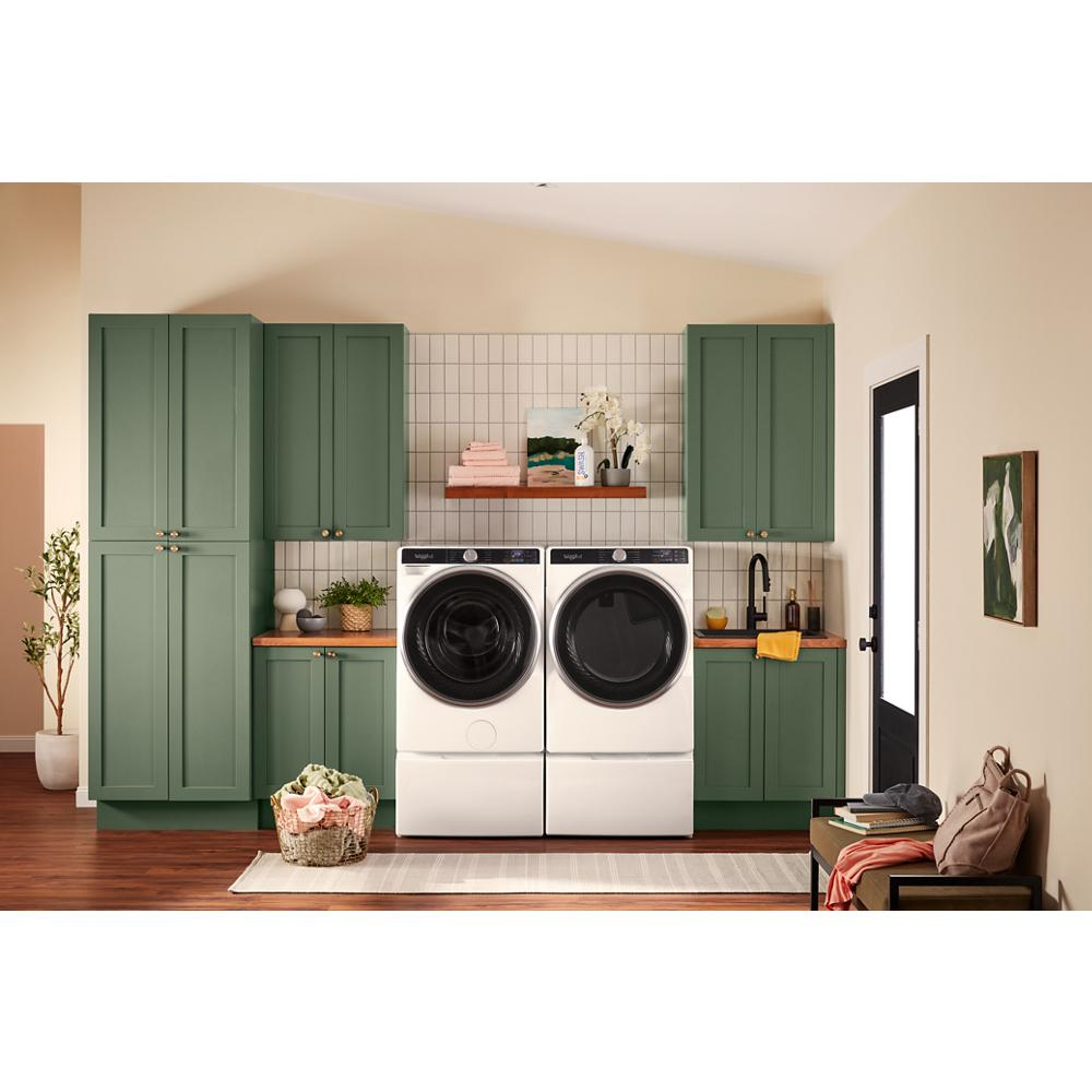 Laundry room with green cabinetry featuring white front load washer and dryer, countertop decor, and wall-mounted shelf with plants and towels