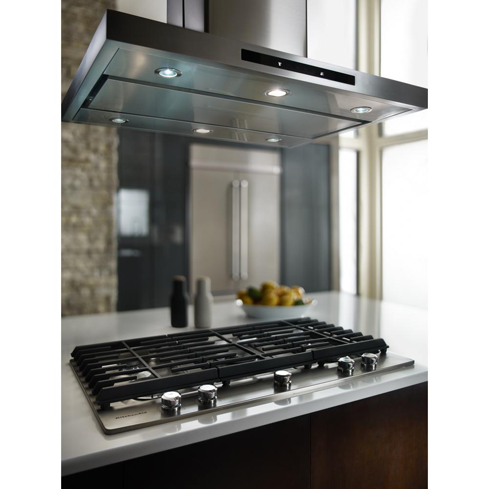 Stainless steel island-mount canopy hood with built-in LED lights above gas cooktop in modern kitchen setting