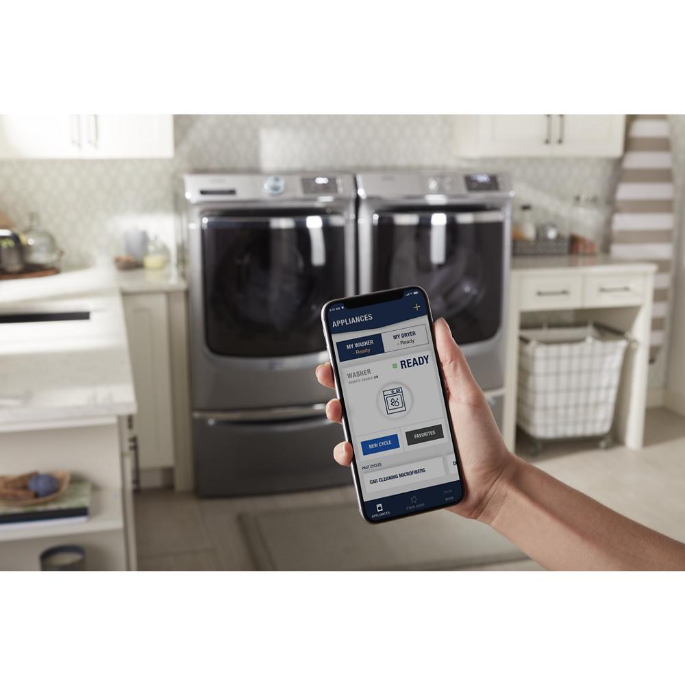 Hand holding smartphone displaying appliance app in modern laundry room with front load washer and dryer pair