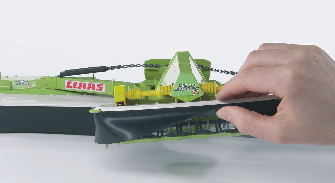 Hand adjusting the black protective cover of a green Bruder Claas Disco model mower in toy collections under $100