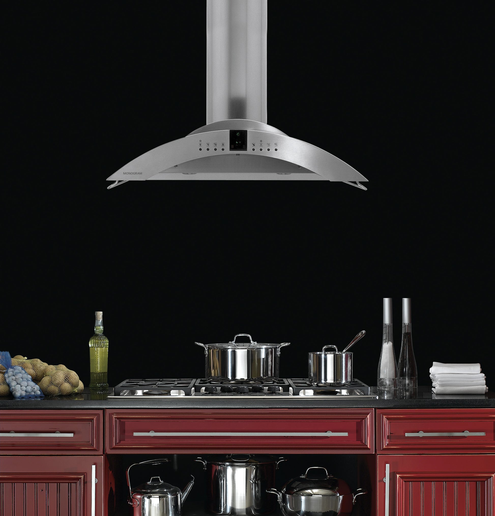 Stainless steel island vent hood with curved canopy and digital controls above red kitchen cabinetry in appliances collection