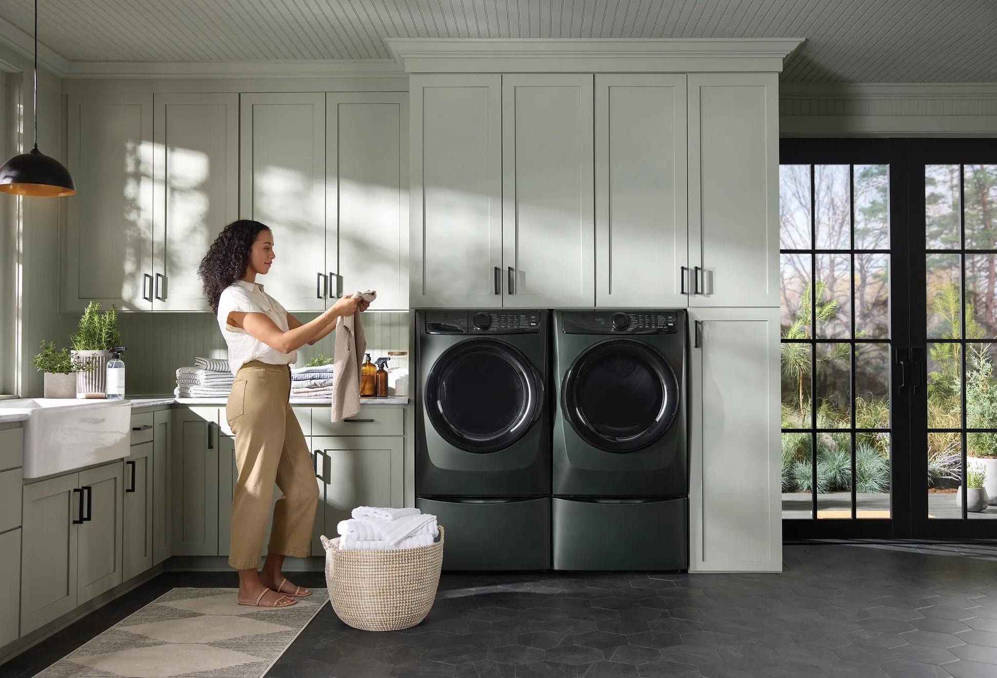 Woman in modern laundry room with dark green front load electric washer and dryer from washers and dryers collection