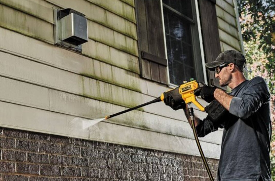 Man using a yellow cordless power cleaner to wash exterior siding during home improvement work