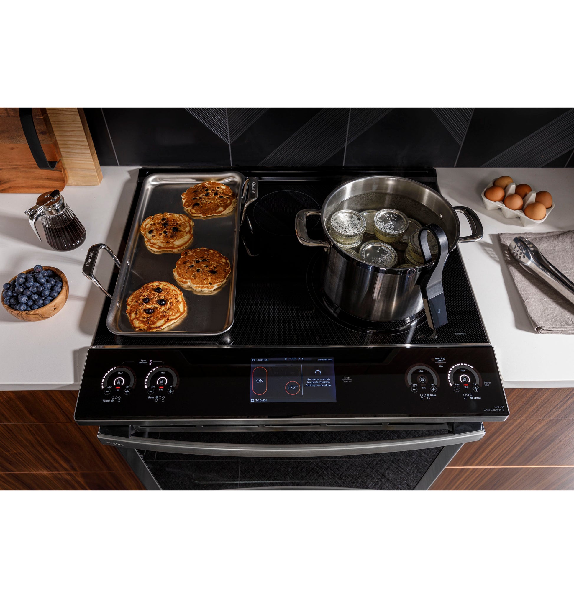 Black induction cooktop with convection range cooking pies and boiling jars in stainless steel pot in modern kitchen