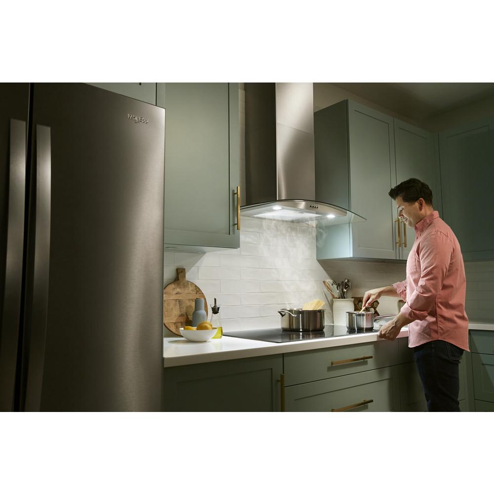 Man cooking on stovetop under stainless steel curved glass wall mount range hood in modern kitchen setting