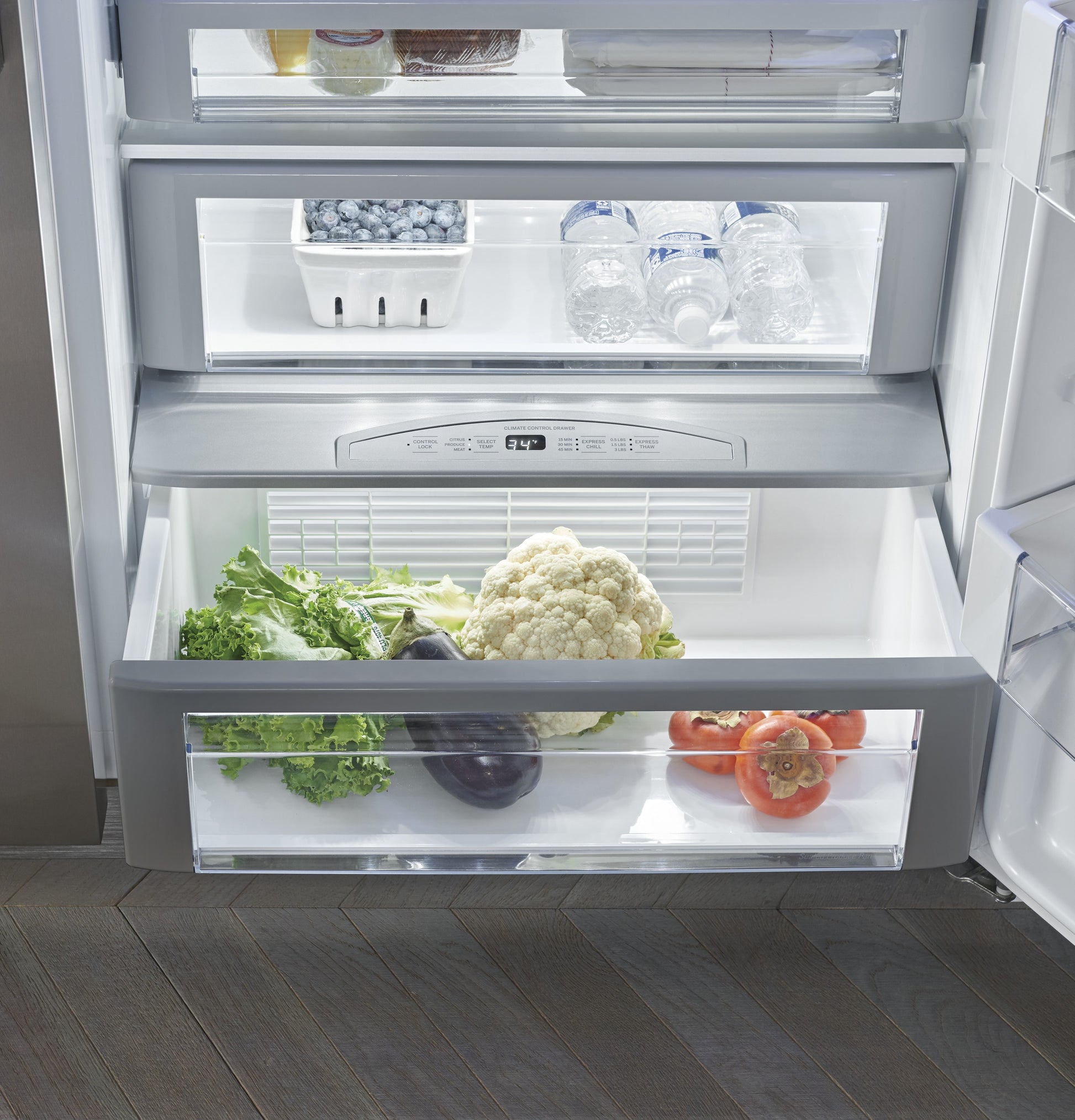 Open door view of a stainless steel built-in side-by-side refrigerator interior with fresh produce and bottled water