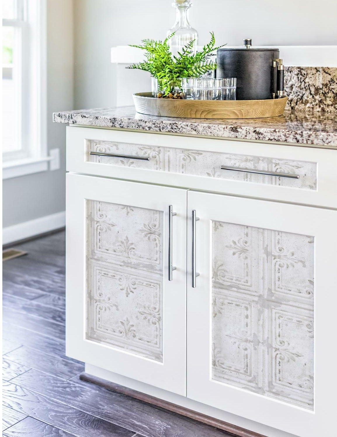 White kitchen cabinet doors and drawer fronts decorated with embossed vintage tin tile peel-and-stick wallpaper panels