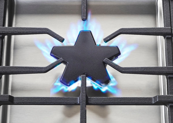Close-up of star-shaped burner with blue flame on stainless steel gas cooktop from Thermador Appliances collection