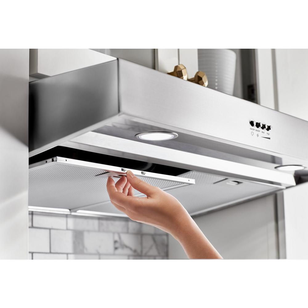 Hand removing stainless steel grease filter from illuminated range hood vent in modern kitchen setting