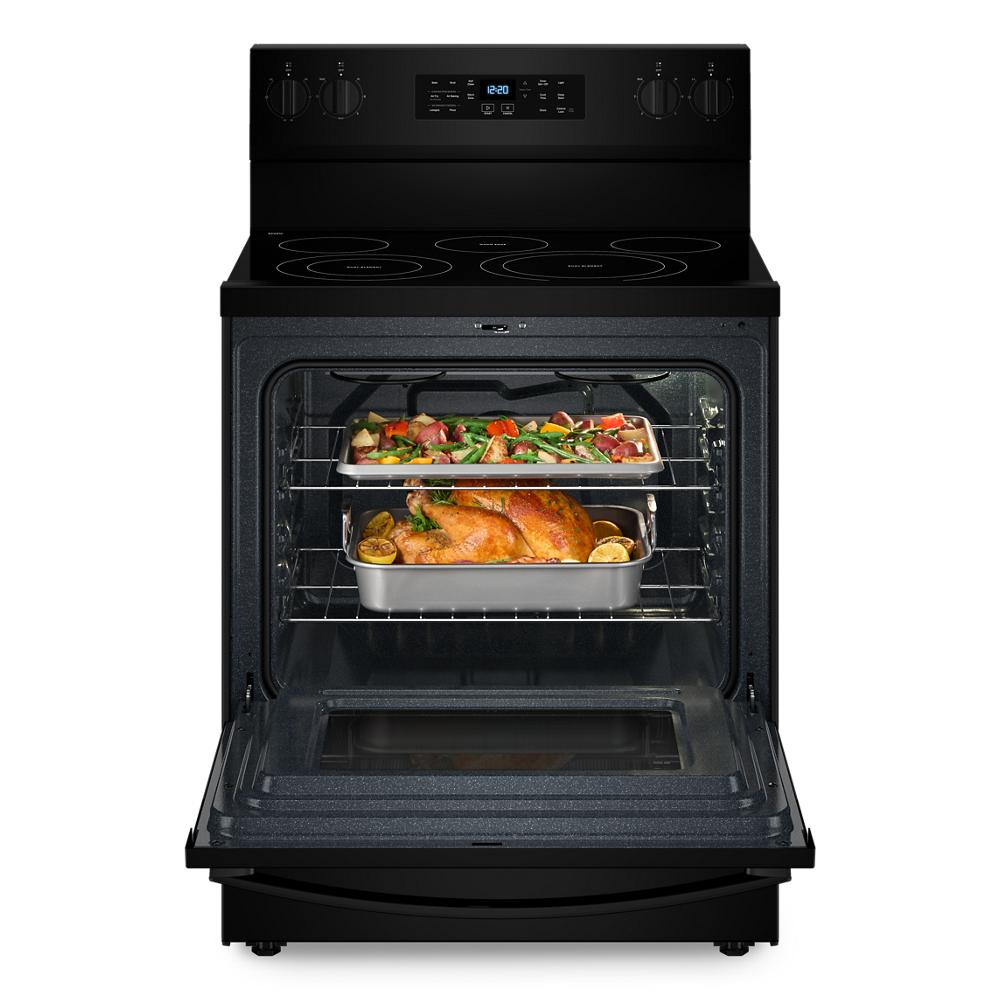Black electric range with open oven containing roasting pan with cooked chicken and tray with vegetables on middle racks