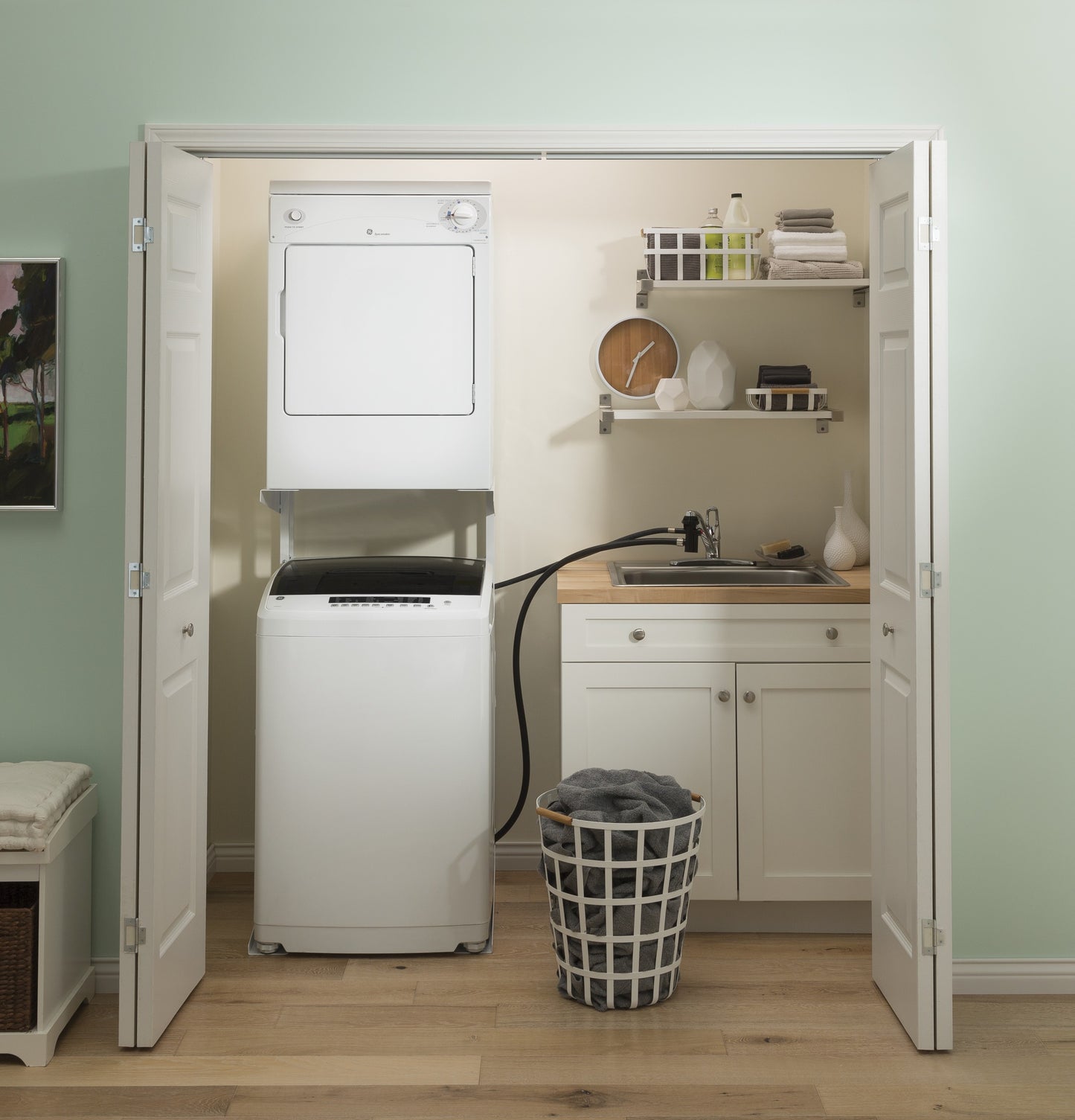 Compact laundry closet featuring stacked washer and dryer, white cabinetry, and organized laundry essentials on shelves