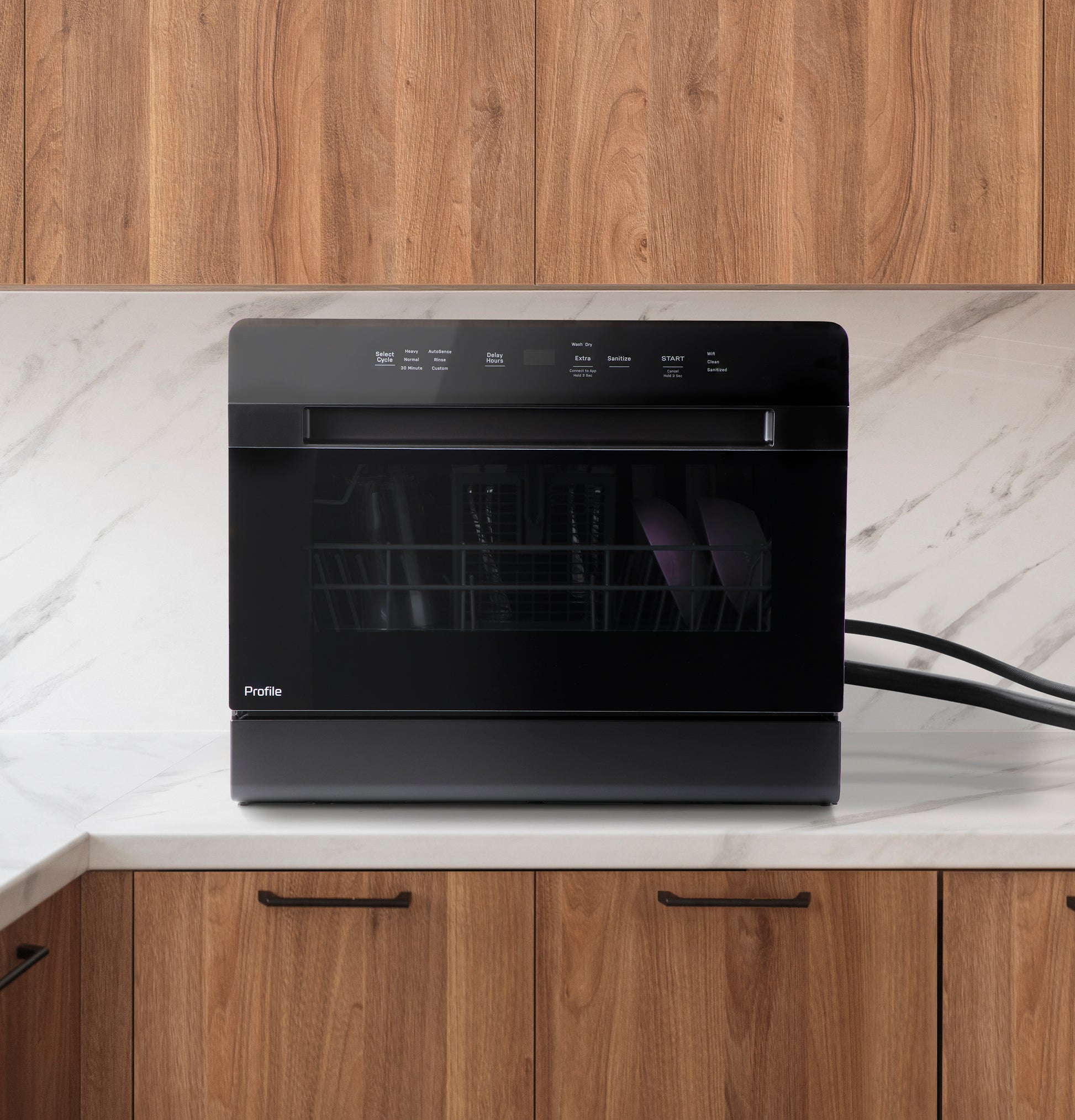 Black compact dishwasher with digital touch controls on marble countertop in modern kitchen setting