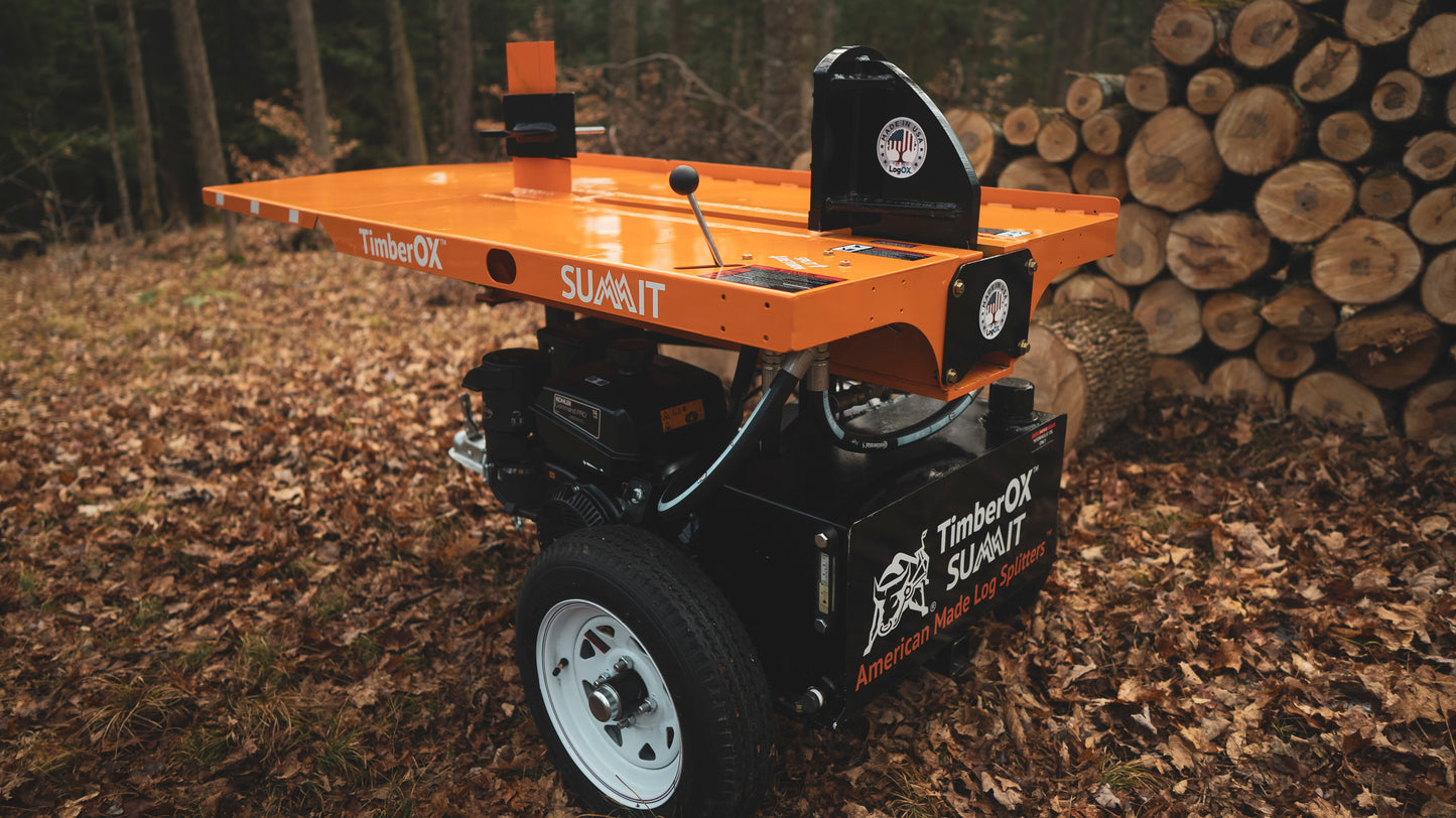 Orange and black log splitter with white wheels on forest ground near stacked cut logs for outdoor wood splitting tasks