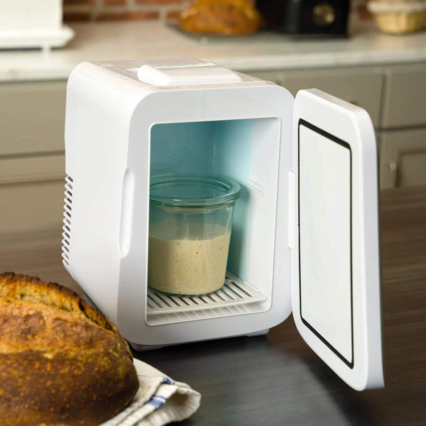 Compact white kitchen appliance with open door holding a glass jar of sourdough starter on wooden countertop