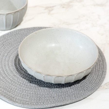 White ceramic bowl with subtle speckled design on a textured gray placemat on marble surface