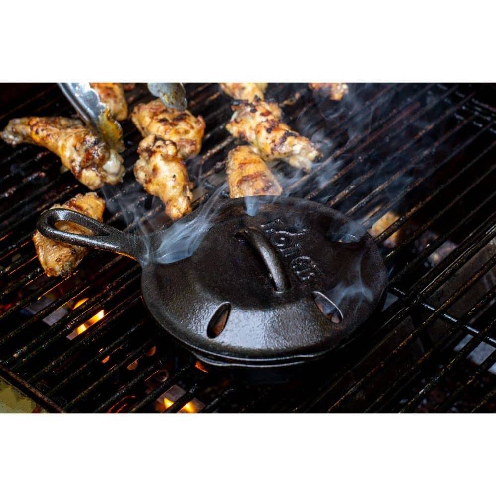 Black cast iron smoker skillet with vented lid releasing smoke on grill with chicken wings cooking nearby in kitchenware collections