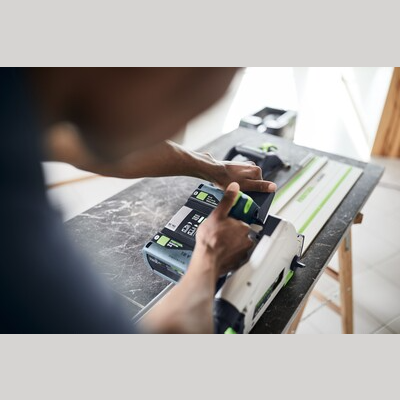 Person attaching battery to Festool cordless track saw on workbench for power tools and home improvement