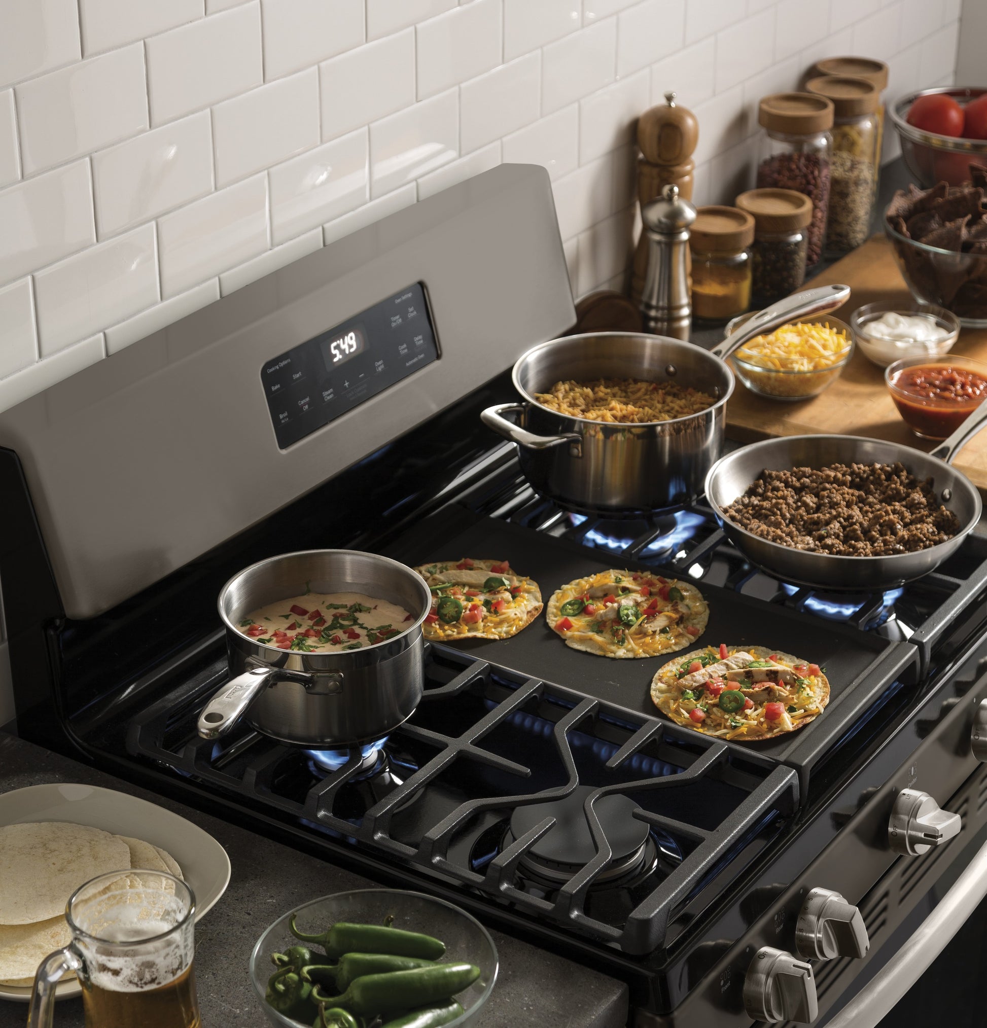 Black free-standing gas range cooktop with pots, pans, and mini pizzas cooking in a kitchen and home appliance setting
