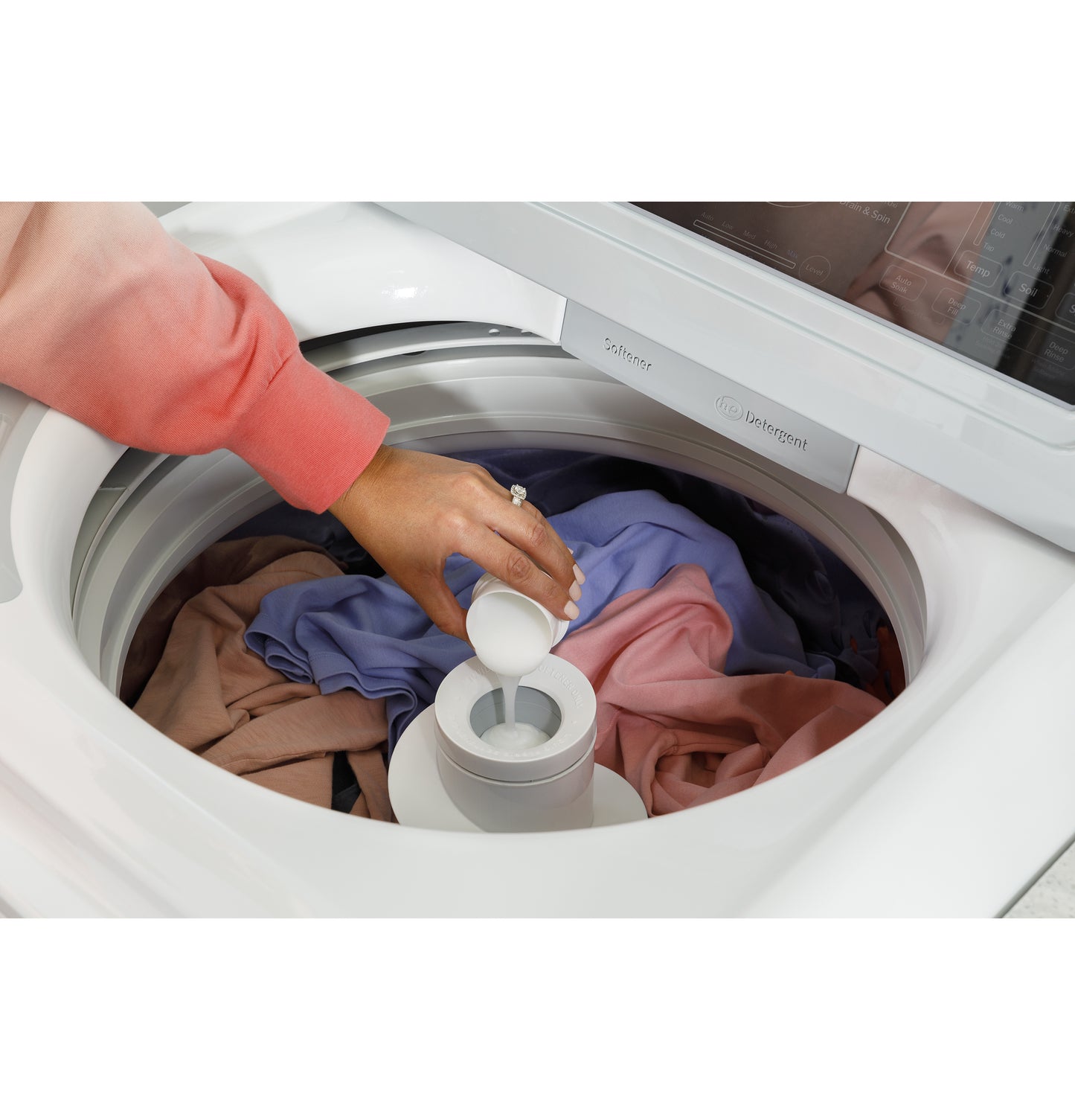 Hand adding detergent into the center dispenser of a white top load washer filled with mixed laundry colors from Washers collection