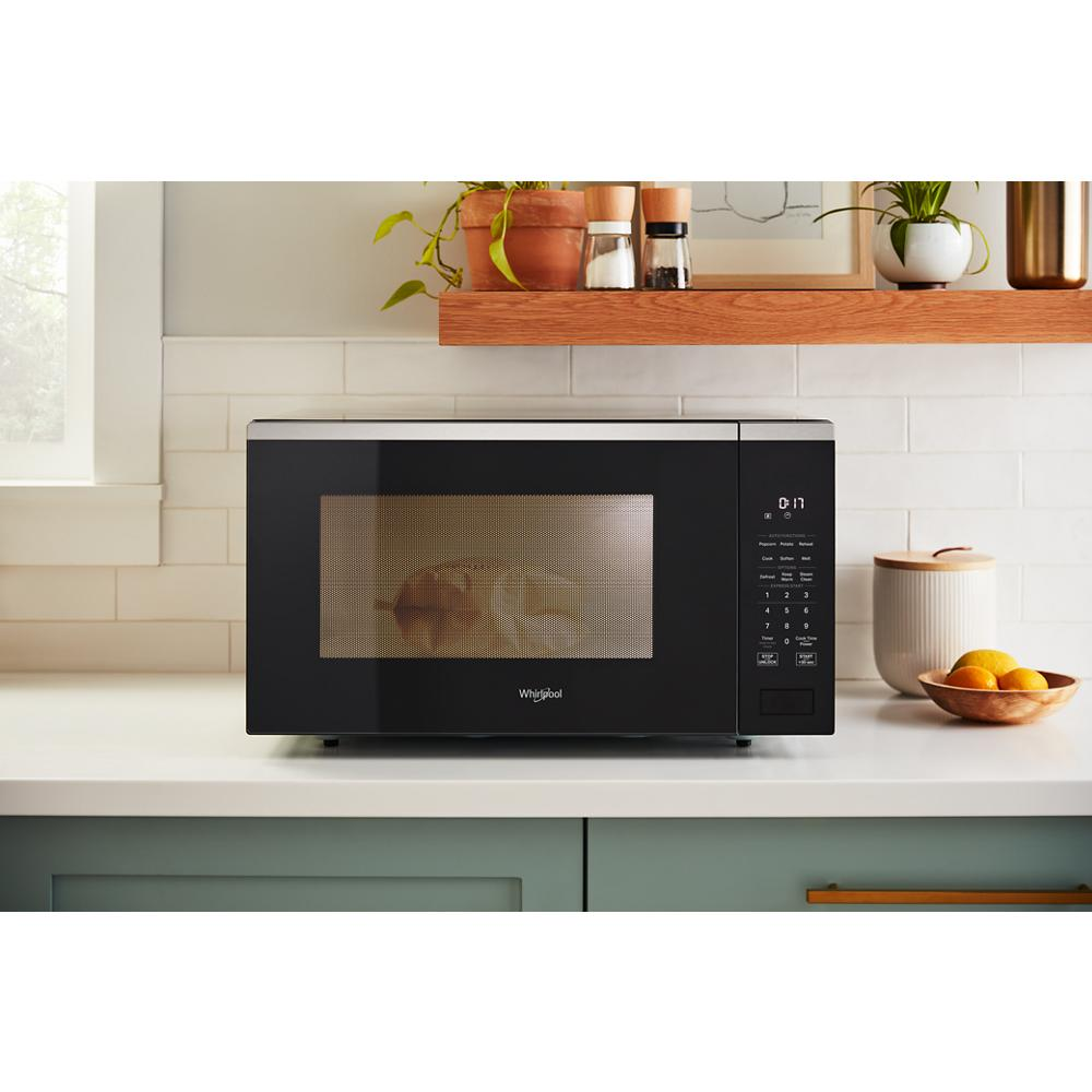 Black sensor cooking microwave with digital control panel on white kitchen countertop with decor items