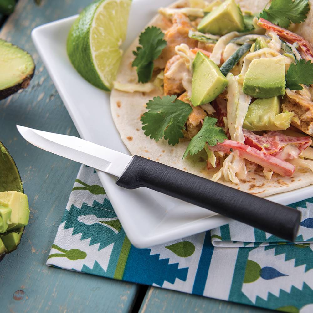 Sharp peeling paring knife with black handle resting beside a fresh taco topped with avocado and cilantro leaves