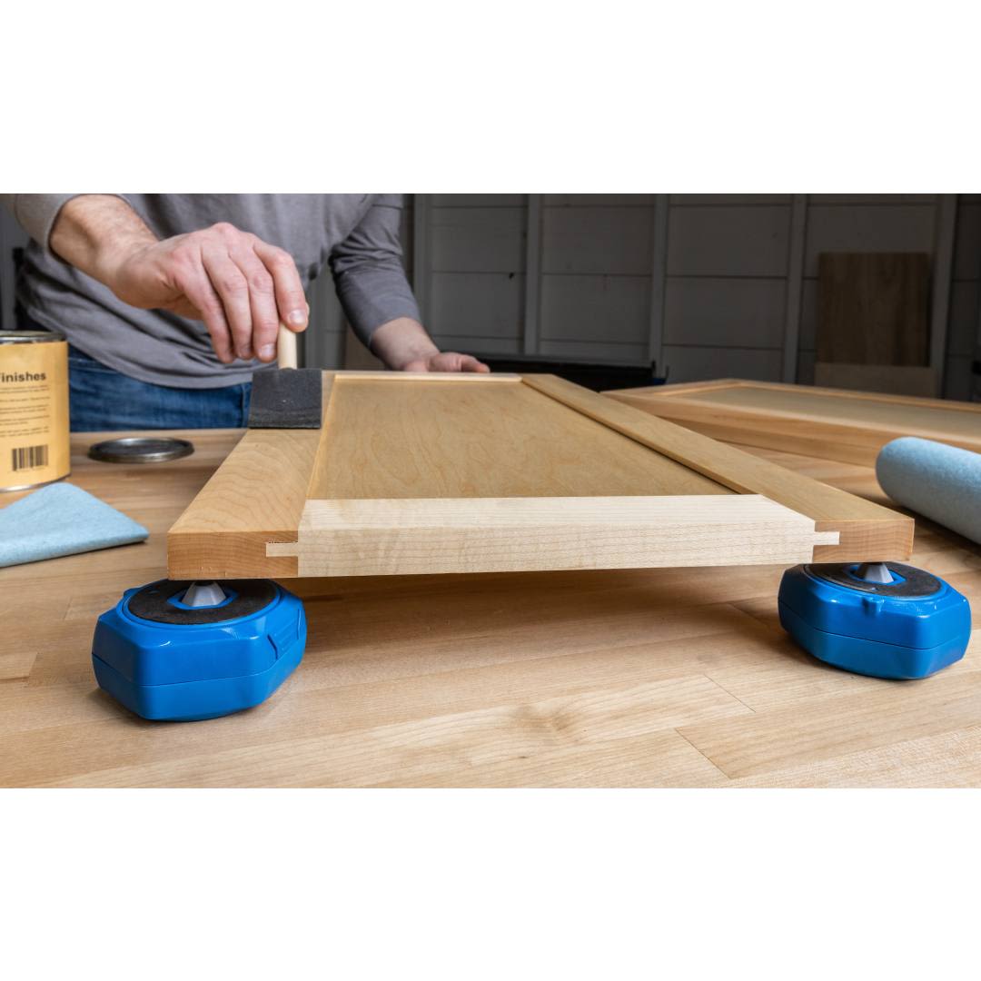 Blue project blocks supporting a wooden panel while a person applies finish in tools and home improvement setting