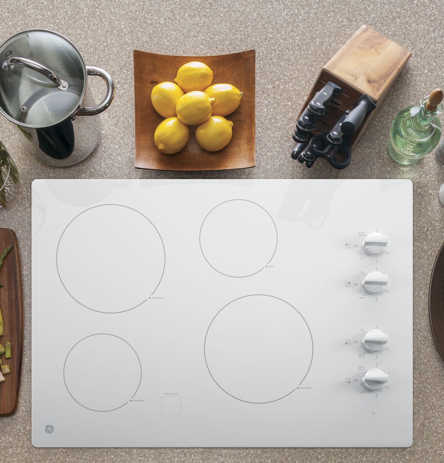 White built-in electric cooktop with four burners and knob controls, styled with kitchenware and lemons nearby