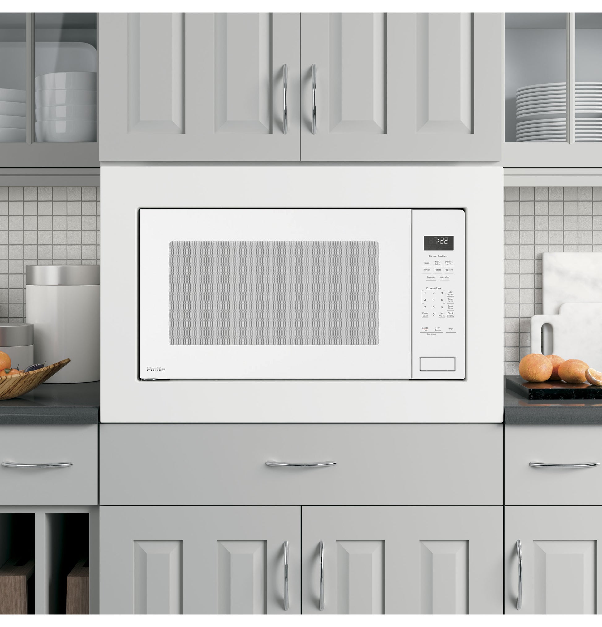 Built-in white microwave oven with digital sensor controls set within gray kitchen cabinetry and tiled backsplash
