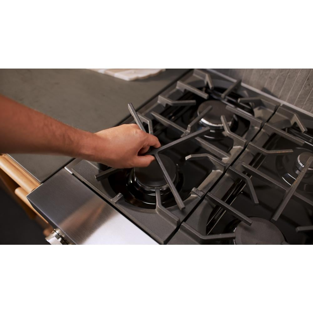 Hand adjusting black cast iron grate on a stainless steel six-burner commercial-style gas range in modern kitchen